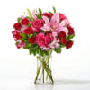 Bouquet of pink lilies, red roses, and carnations in a clear glass vase