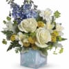 Bouquet of white roses, blue flowers, and yellow blooms in a glass cube vase