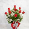Red roses arranged in a glass vase with white baby's breath and ribbon