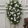 Standing spray of white carnations and baby's breath with white ribbon bows on a wooden easel.