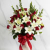 Red roses and white lilies arranged in a decorative vase with a red ribbon