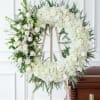White floral funeral wreath on a wooden easel beside a casket