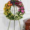 Colorful floral wreath on a standing easel beside a casket