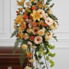 Tall standing spray with yellow lilies and peach roses on an easel beside a wooden casket.
