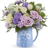 Lavender and white roses and mums arranged in a blue daisy-print ceramic pitcher