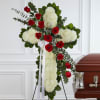 Red roses and white flowers arranged on a standing cross beside a casket