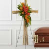 Floral cross on an easel beside a casket