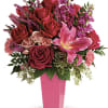 Tall pink vase with red and pink roses, a pink lily, carnations, stock, and a succulent.