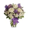 White roses and purple flowers in a clear glass vase with a purple ribbon