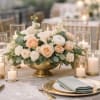 Low centerpiece of peach and white roses in a gold bowl surrounded by glass candles on a wedding table
