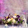Low floral arrangement of purple, white, and peach blooms in a white vase
