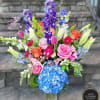 Tall mixed bouquet with pink roses, lilies, blue hydrangea, and purple delphinium in a clear vase