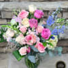 Mixed bouquet of pink and white roses with blue delphinium in a clear glass vase.