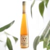 A tall bottle of honey with a label, framed by blurred green leaves.