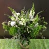 Tall green and white floral arrangement with snapdragons and roses in a clear glass cylinder vase