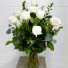 White roses arranged in a clear glass vase with mixed greenery
