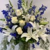 White lilies and cream roses arranged with blue flowers in a glass vase.