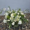 Loose white and cream flower arrangement with greenery in a clear glass vase on river stones