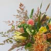 Asymmetrical arrangement with peach dahlias, yellow lilies and orange protea in a vase against a light background