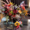 Colorful mixed floral arrangement with fruit accents in a dark vase