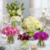 Four floral centerpieces in glass vases on a set table