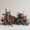 Low holiday centerpiece with evergreen branches, red berries, and black candles