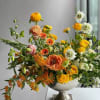 Mixed orange, yellow, white, and peach flowers in a silver pedestal vase