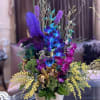 Tall colorful floral arrangement in a gold vase with orchids and feathers