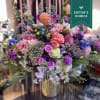 Mixed pink, purple, and peach flowers in a gold vase