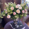 Blush roses and pale green flowers arranged in a glass vase on a table