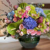 Colorful bouquet in a green glass vase with hydrangeas, roses, and orchids