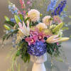 Mixed bouquet of pastel and blue flowers in a white pedestal vase
