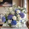 Blue hydrangeas and white orchids arranged in a white bowl vase