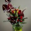 Dark red anthuriums and red flowers in a glass vase with eucalyptus
