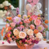Pastel flower arrangement in a wicker basket with pink balloons behind it