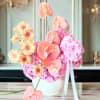 Pink and peach floral arrangement in a white vase with ribbon
