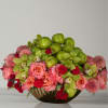 Pink and red floral arrangement with green apples in a low vase