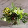 Green floral arrangement with orchids, lilies, and pinecones in a glass vase