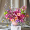 Pink and purple floral arrangement in a pale pink vase