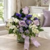 Lavender roses and white lilies in a glass vase with a purple ribbon