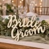 Bride Groom sign surrounded by white roses and greenery on a table centerpiece