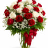 Red and white roses in a clear glass vase with a red ribbon