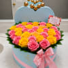 Heart-shaped box of pink and yellow roses with a pink ribbon