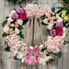 Heart-shaped floral wreath with pink hydrangeas, roses, and lilies on a wooden stand