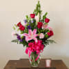 Mixed bouquet of pink lilies, red roses, and purple flowers in a glass vase