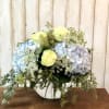 Blue and lavender hydrangeas with pale yellow roses in a glass vase