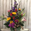 Tall mixed bouquet in a glass vase with roses, lilies, orchids, and yellow daisies