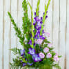 Tall floral arrangement with purple flowers and pale pink roses in a square vase