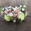 Low floral centerpiece with peach and white roses and pale green hydrangeas in a silver vase