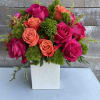 Pink and coral roses arranged in a white square vase